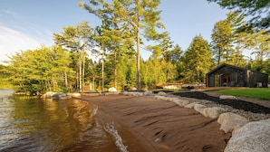 A lakeside property with a sandy beach, a stone pathway, and a cabin with a glass door. - Nalu Retreat Lakeside (Porters Lake)