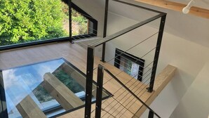 Un intérieur à plusieurs niveaux avec un plancher en verre donnant sur un espace extérieur, un escalier avec des rampes en métal et une verrière.