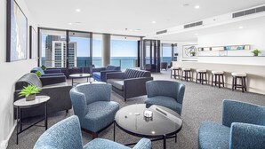 Et moderne loungeområde med siddepladser, en bar og udsigt over byen og havet.