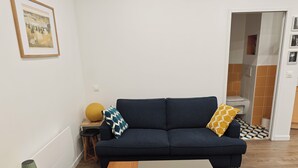 A living room with a dark blue sofa, a wooden coffee table, a yellow lamp, and a framed picture on the wall.