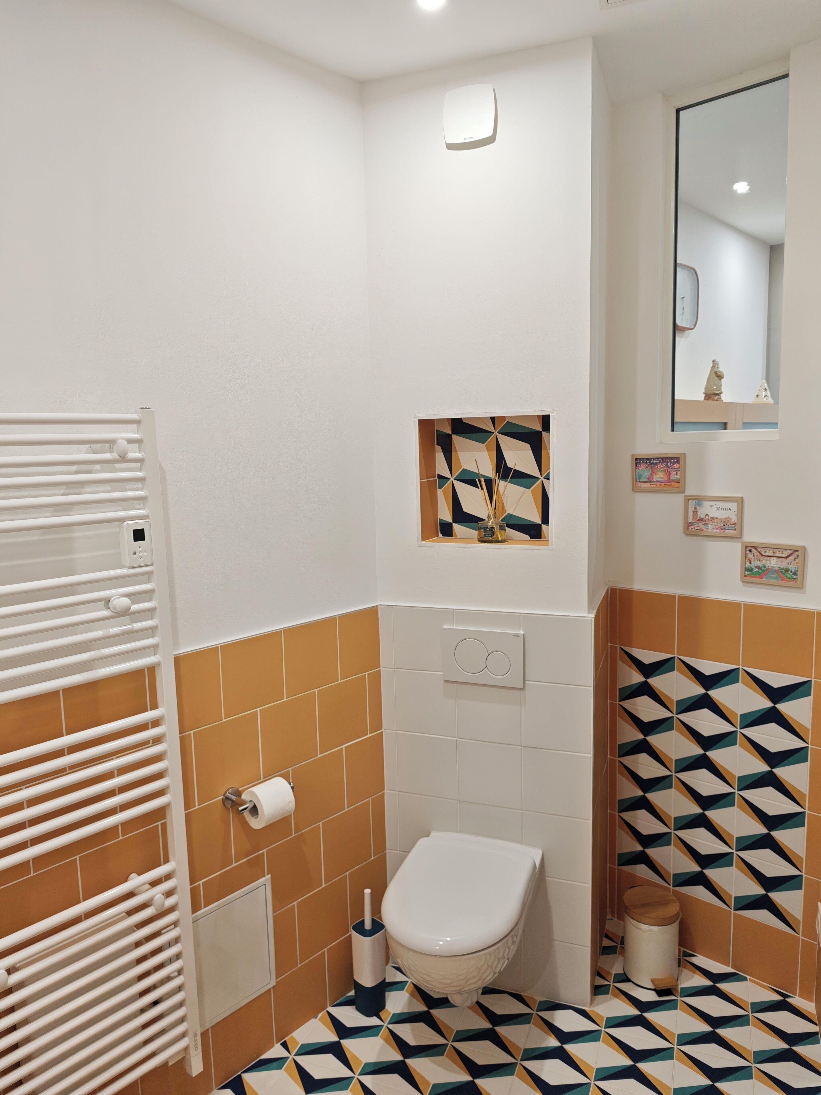 A bathroom with a toilet, a towel rack, a mirror, and a wall-mounted heater.