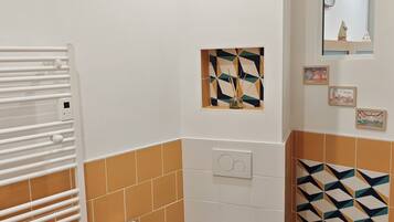A bathroom with a toilet, a towel rack, a mirror, and a wall-mounted heater.