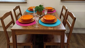 A dining table set with orange plates, blue placemats, and clear glassware, flanked by wooden chairs, with a framed picture on the wall above. - La maison de violette "studio haut standing (Montdidier)