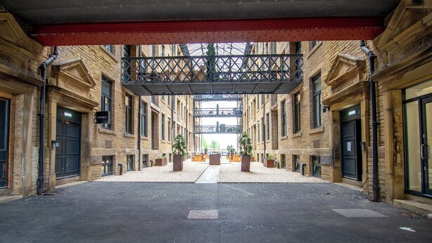 A covered courtyard with a central walkway, surrounded by brick buildings with "Warehouse" signs, and potted plants at the corners.