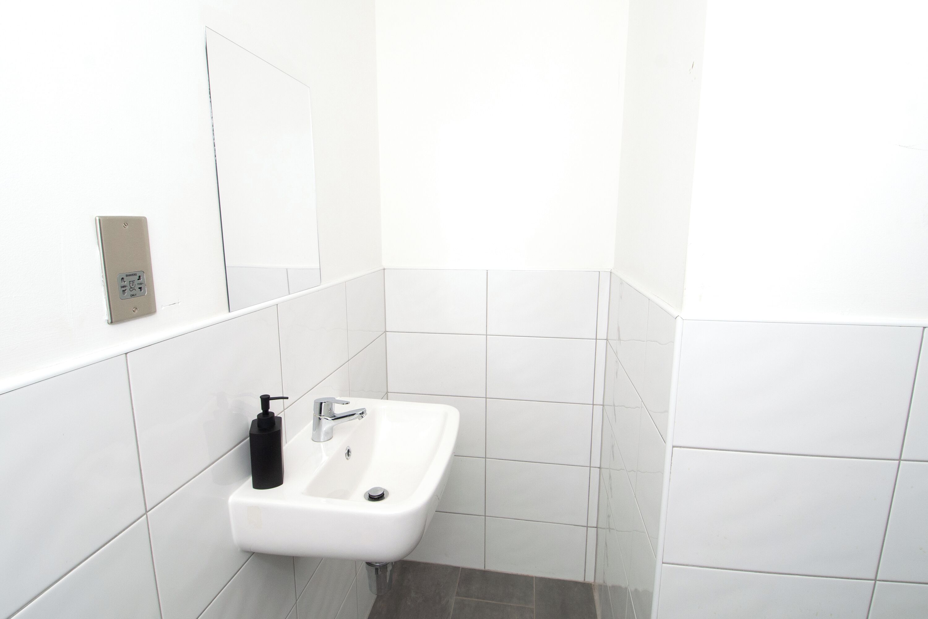 Un bagno con un lavandino bianco, uno specchio e una presa elettrica a muro.