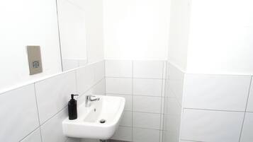 Un bagno con un lavandino bianco, uno specchio e una presa elettrica a muro.