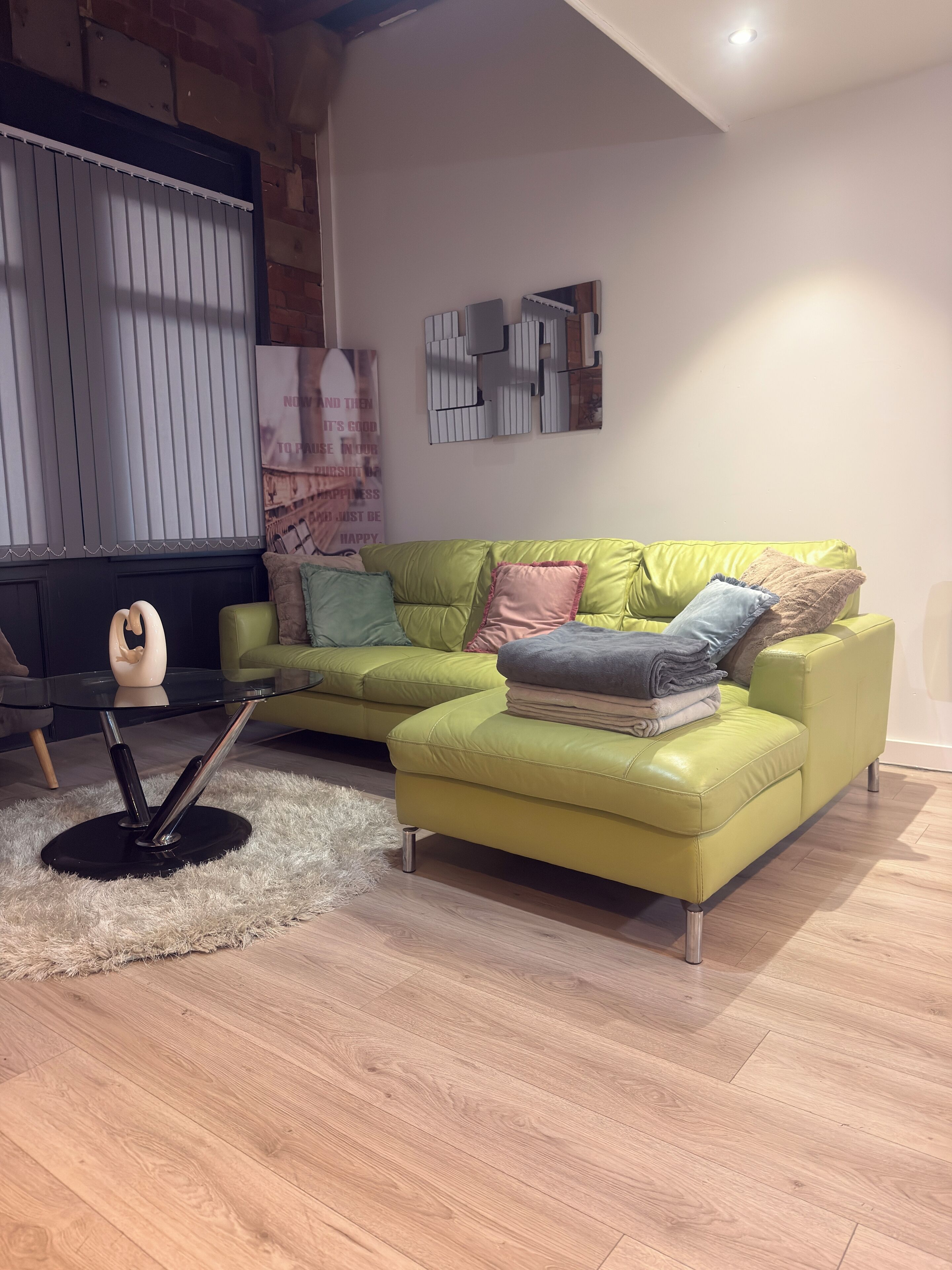 A living room with a green sofa, a glass coffee table, and a decorative sculpture.