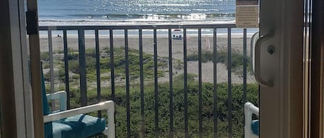 A view through a glass door to a balcony with a beach and ocean.