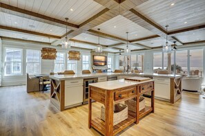 A spacious kitchen with a large island, wooden ceiling beams, and large windows offering a view of the beach.