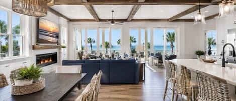 A spacious living area with a large sofa, dining table, and chairs, a fireplace, and a view of the ocean.