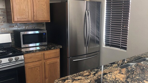 Una cocina moderna con armarios de madera, electrodomésticos de acero inoxidable, encimeras de granito y una ventana con persianas.