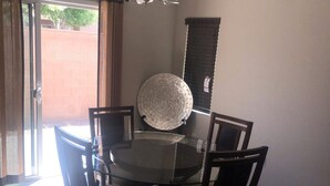 Un comedor con una mesa de vidrio rodeada por cuatro sillas, una lámpara de araña y un plato decorativo en la pared.