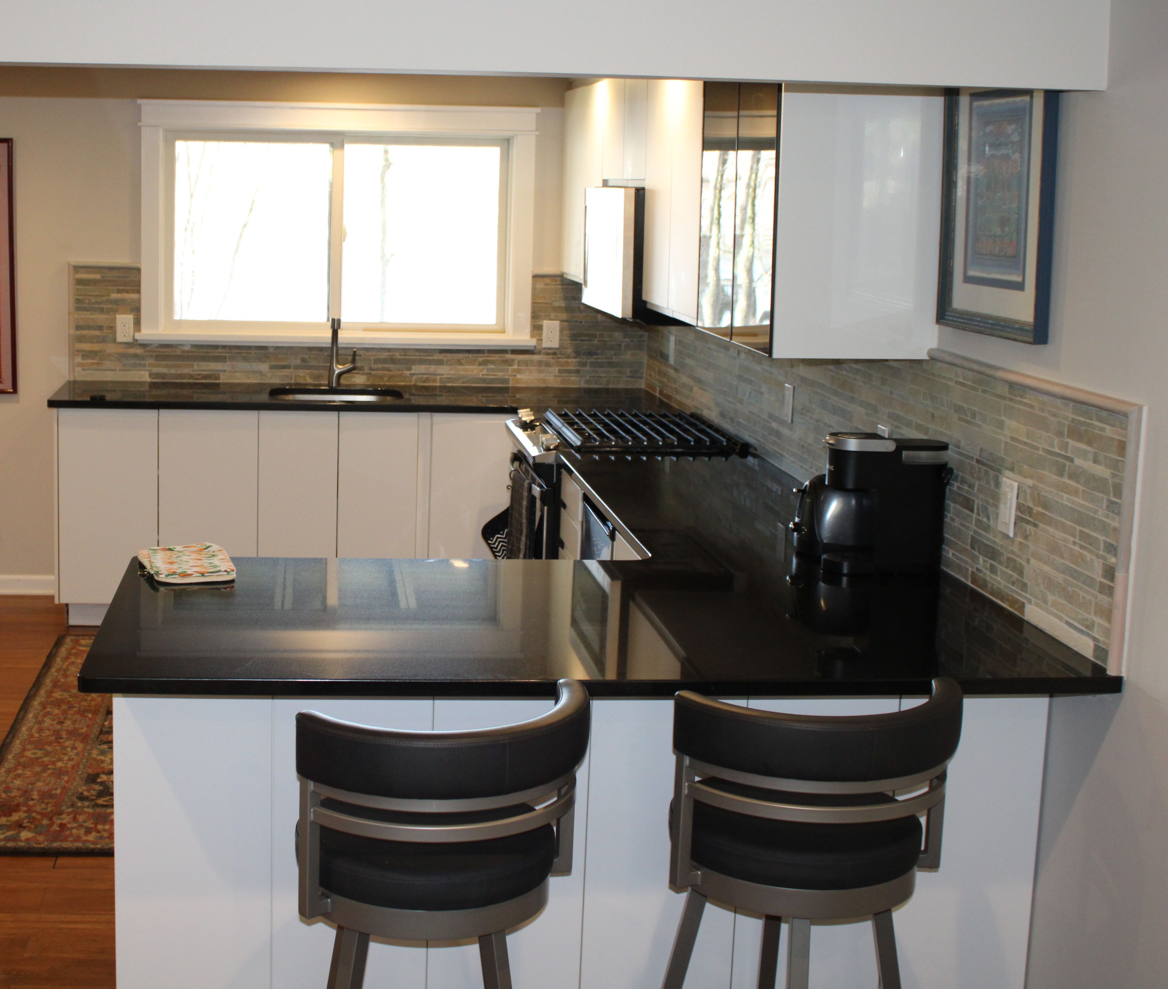 A modern kitchen with a black countertop, white cabinets, a double sink, and a coffee maker. There are two bar stools at the counter.