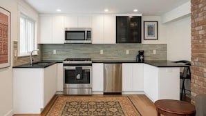 A modern kitchen with white cabinets, stainless steel appliances, a patterned rug, and a brick accent wall. - Spacious Lakeside Hideaway (Newtown)
