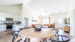 Een moderne keuken met witte kasten, een eethoek met een ronde tafel en stoelen, en een woonkamer met een bank en salontafel.