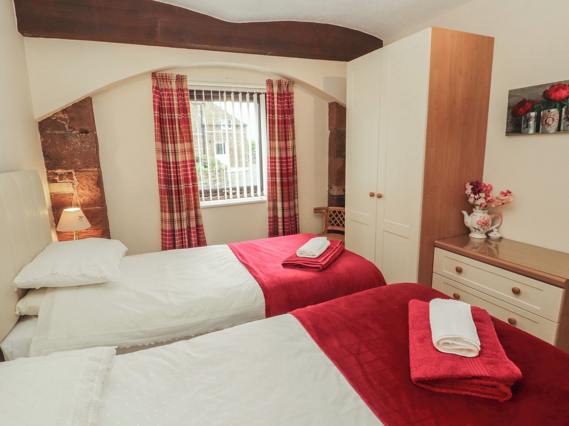 A hotel room with two beds, a wooden dresser, a mirror, a window with curtains, and a painting on the wall.