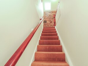 A staircase with a stone wall at the top, carpeted steps, and a wooden handrail.