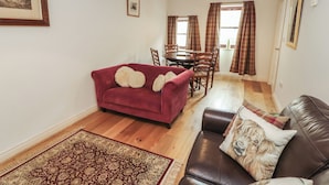 A living room with a red sofa, a brown leather couch, a patterned rug, and a dining area with a table and chairs. - Millers Cottage (Wigton)