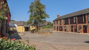 A quiet street with traditional brick buildings, a central tree, and a paved road. - Millers Cottage (Wigton)