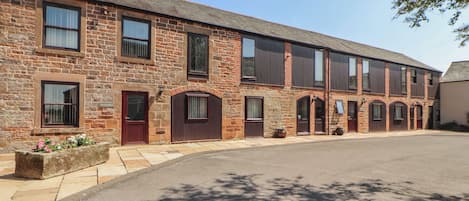A row of brick buildings with multiple doors and windows, a paved street, and a clear sky.
