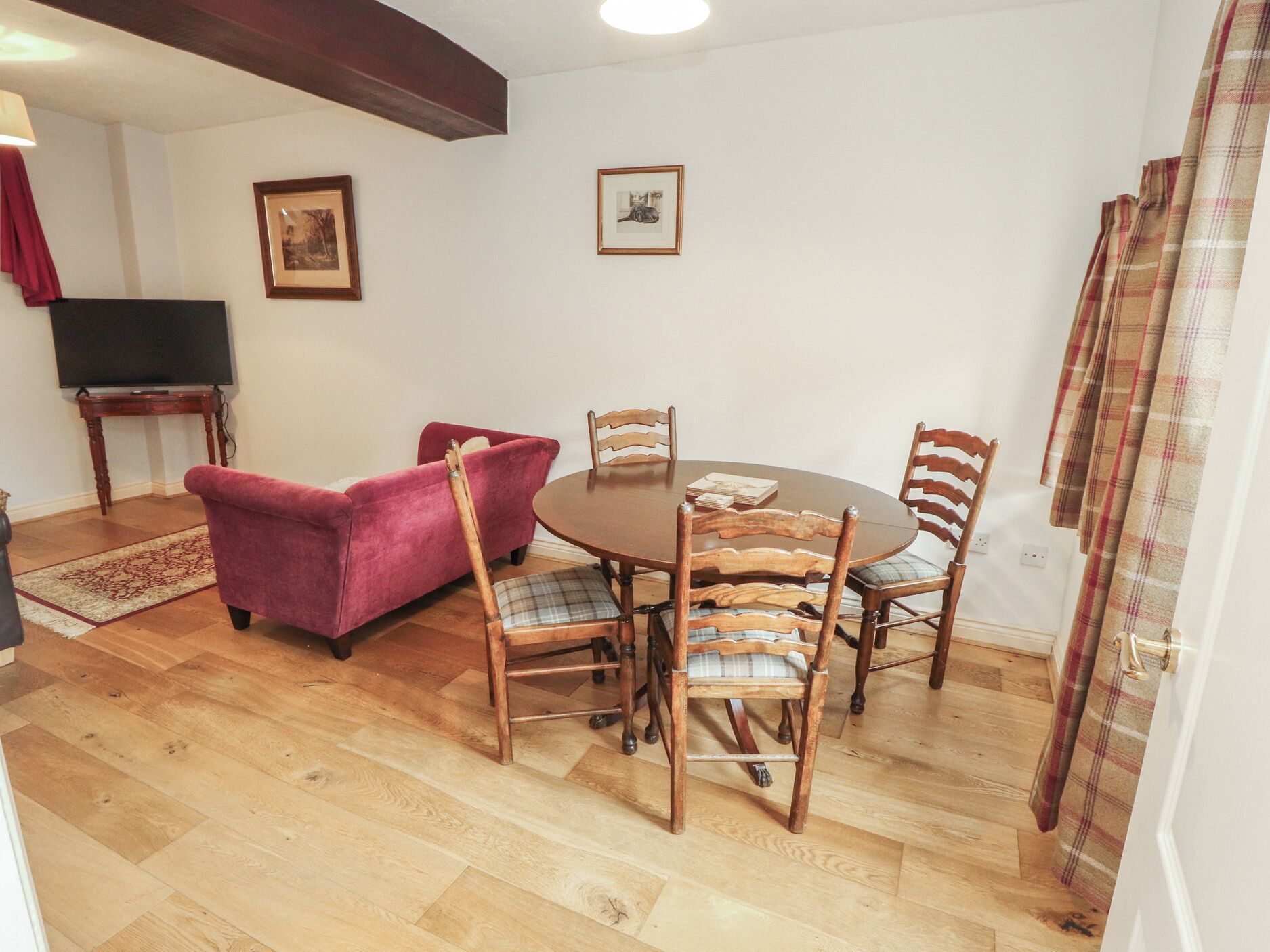 A dining area with a round table and six chairs, a red sofa, a television on a stand, and two framed pictures on the wall.