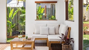 Un patio acogedor con un banco de madera, un sofá blanco y una mesa con bebidas y aperitivos.