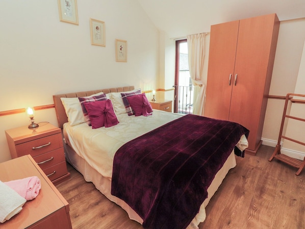 A bedroom with a bed, a nightstand, a wardrobe, and a window with curtains.