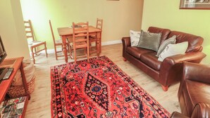 Ein Wohnzimmer mit einem Holzesstisch, einem braunen Ledersofa und einem gemusterten Teppich.