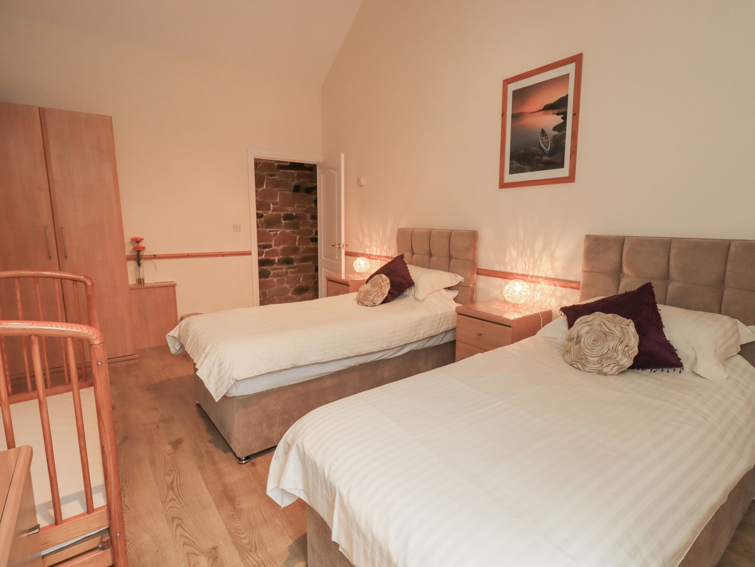 A bedroom with two beds, a wooden chair, a stone wall, and a framed picture on the wall.