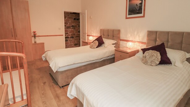 A bedroom with two beds, a wooden chair, a stone wall, and a framed picture on the wall. - The Hayloft (Wigton)
