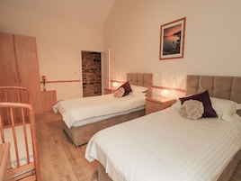 A bedroom with two beds, a wooden chair, a stone wall, and a framed picture on the wall.