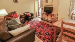 A living room with a brown leather sofa, a wooden dining table, and a television on a stand. - The Hayloft (Wigton)