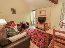 A living room with a brown leather sofa, a wooden dining table, and a television on a stand.