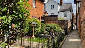 A narrow alleyway with brick houses, a metal fence, and a small garden area. - Historic 1Bd Cottage In Heart Of Farnham (Farnham)