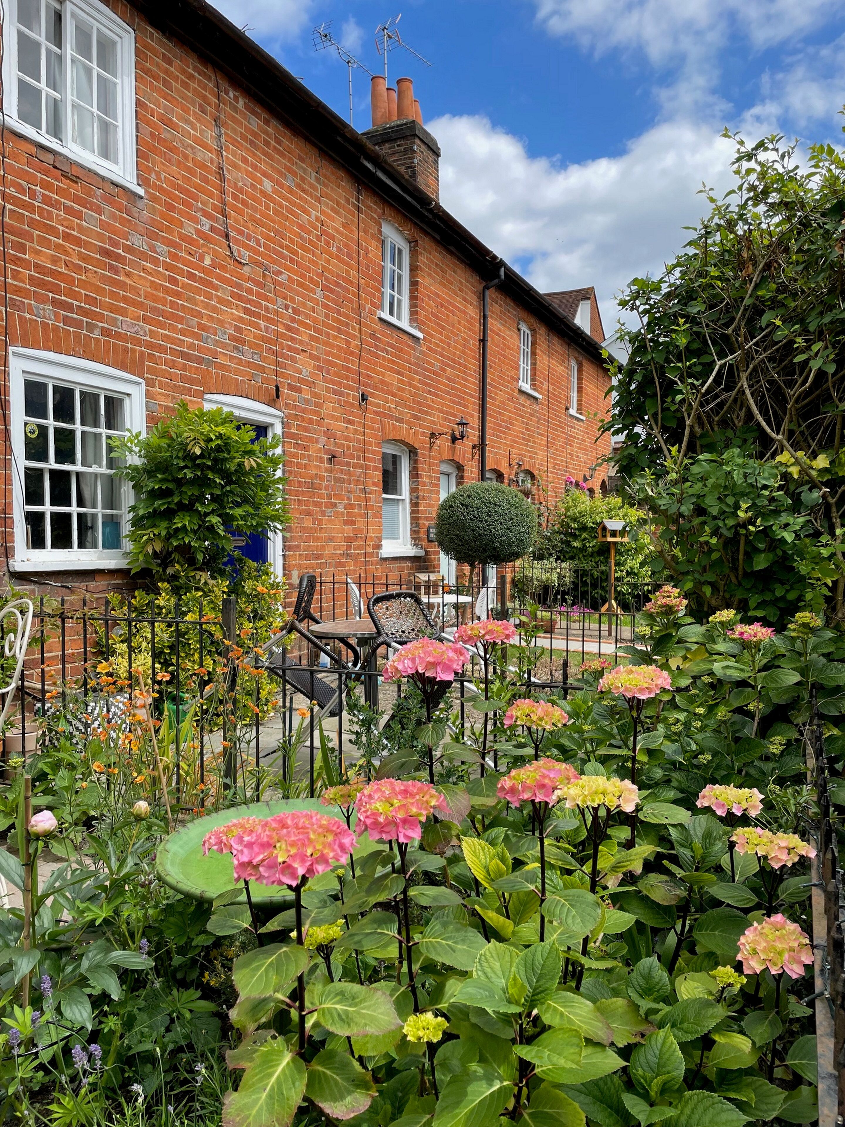 Una casa in mattoni con un giardino adornato da ortensie rosa e diverse piante.
