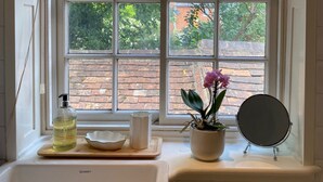 A bathroom with a window, a bottle of Baylis & Harden's hand wash, a bowl, a potted orchid, and a round mirror. - Historic 1Bd Cottage In Heart Of Farnham (Farnham)