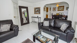 Uma sala de estar com dois sofás de couro preto, uma mesa de centro de vidro e uma área de jantar ao fundo.