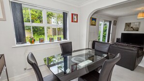 Uma sala de jantar moderna com mesa e cadeiras de vidro, um sofá e uma televisão na sala de estar.