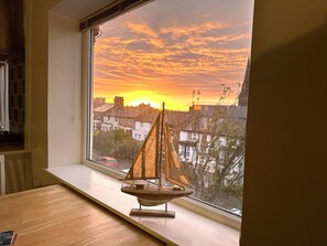 A model sailboat on a windowsill with a sunset view of residential buildings. - Bright Seaside Apartment With Stunning River Views (Wallasey)