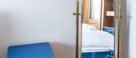 Una mesita de noche azul con un cajón, un espejo de cuerpo entero con marco de latón, y una puerta de madera al fondo.