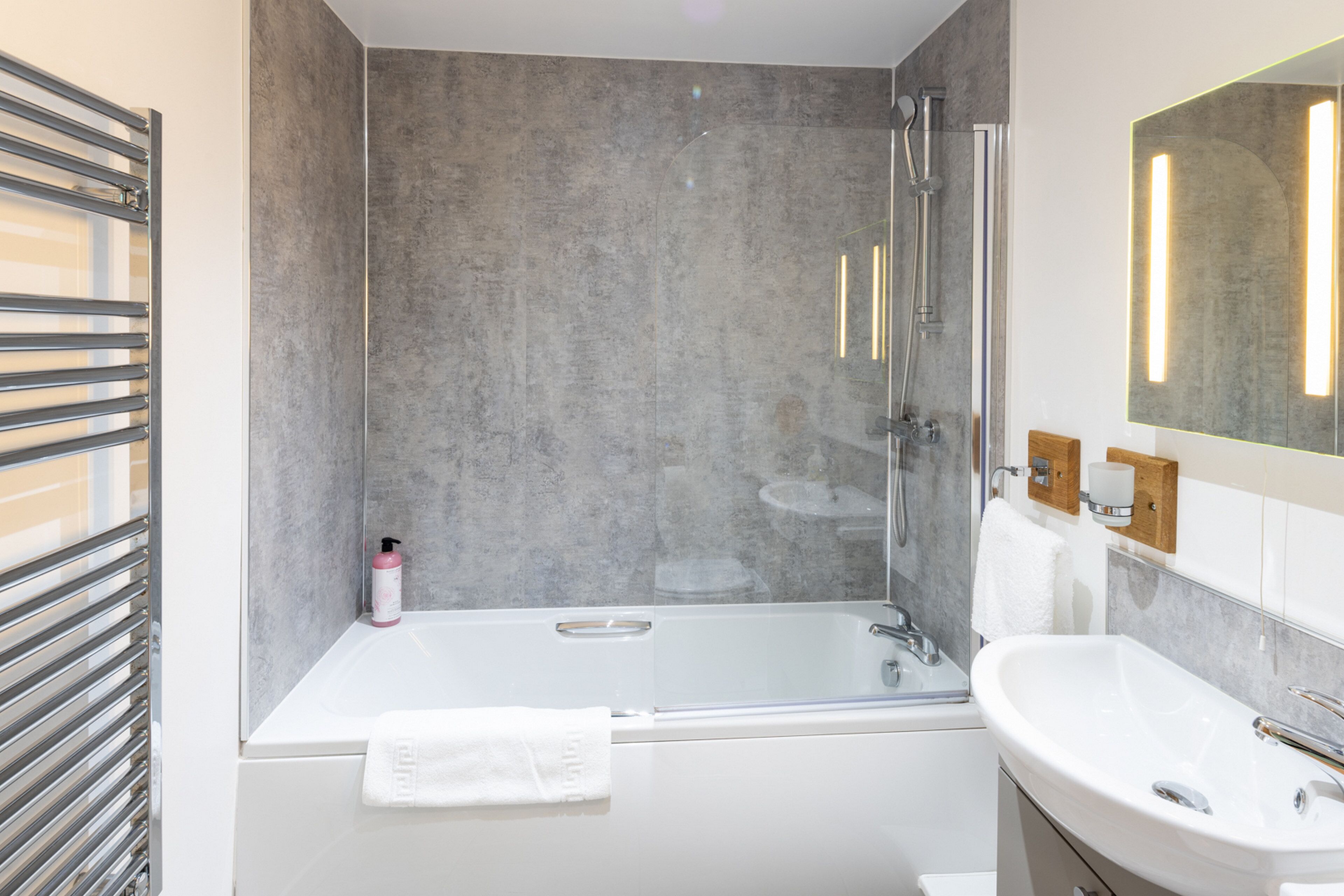 Ein modernes Badezimmer mit einer gläsernen Duschkabine, einer weißen Badewanne und einem Waschbecken mit Spiegel.