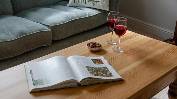 Une table en bois sur laquelle repose un livre ouvert et deux verres de vin rouge.