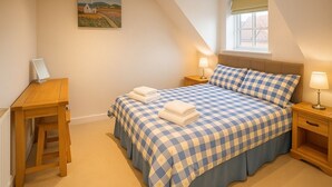 A bedroom with a checkered bedspread, a desk, a lamp, and a painting on the wall. - Elegant 2Bd Townhouse In Thirsk: Cozy & Stylish (Thirsk)