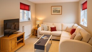 A living room with a sofa, a TV on a wooden stand, a coffee table, and a lamp. - Elegant 2Bd Townhouse In Thirsk: Cozy & Stylish (Thirsk)
