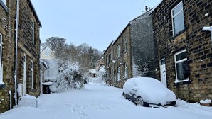 Een smalle straat langs met bakstenen huizen onder een laag sneeuw.
