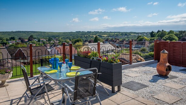 An outdoor patio with a table set for two, surrounded by a garden and a view of the countryside. - 2Bd House With Stunning Views Of The Sea And Gower (Killay)