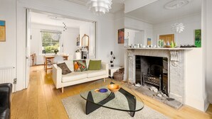 A spacious living room with a fireplace, a dining area, and a modern glass coffee table. - 3Bd Victorian Townhouse Near Norfolk Broads 4A, 2C (Beccles)