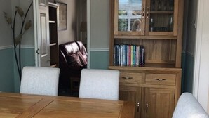 A dining area with a wooden table and four chairs, a cabinet with glass doors, and a hanging light fixture. - Cosy House In Lovely Market Town (Newport)