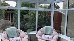 A conservatory with two pink cushioned chairs, each with a pillow labeled "home," and a small bench. - Cosy House In Lovely Market Town (Newport)
