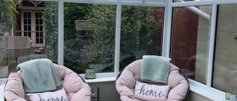 A conservatory with two pink cushioned chairs, each with a pillow labeled "home," and a small bench.